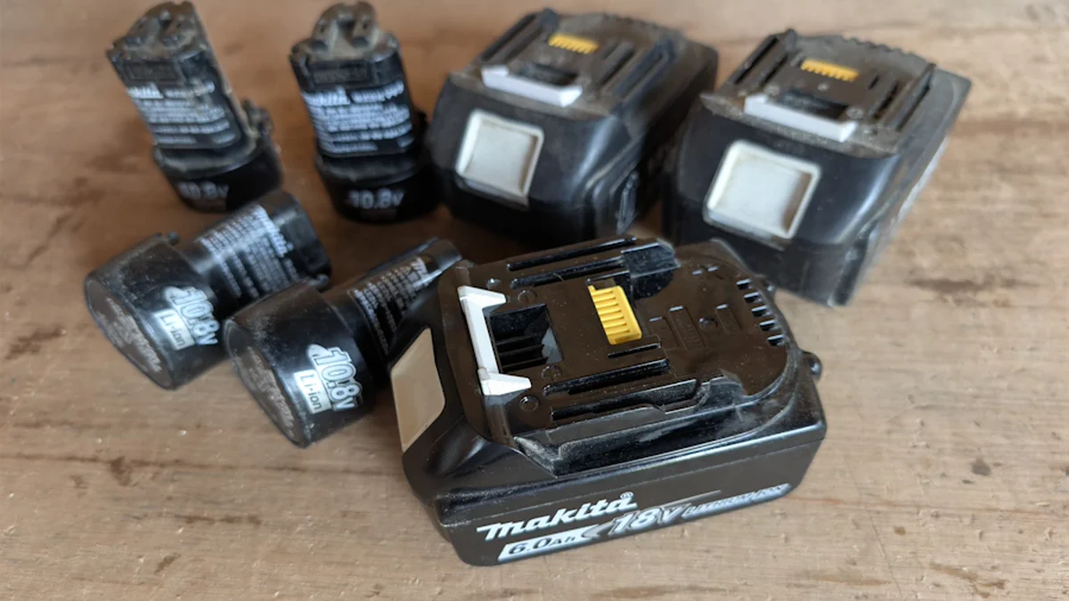 木製の作業台に並べた電圧と形状が異なる6個の工具用バッテリー